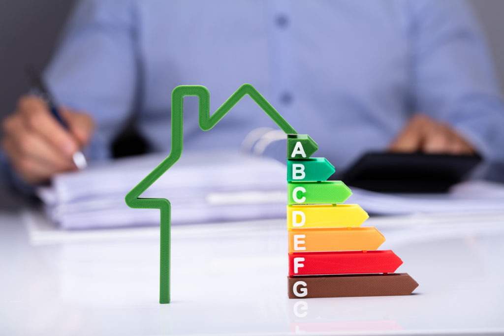 House With Energy Efficiency Rate In Front Of Businesspeople Working On Documents